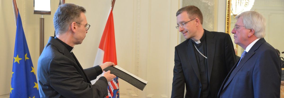  Der künftige Bischof von Fulda, Dr. Michael Gerber (Bildmitte), hat den Treueid vor Hessens Ministerpräsident Volker Bouffier (r.) abgelegt, unterstützt vom Leiter des Kommissariats der katholischen Bischöfe in Hessen, Domkapitular Dr. Wolfgang Pax (l.).   Foto: Hessische Staatskanzlei  