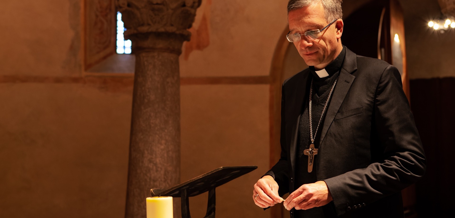 Bischof Dr. Michael Gerber entzündet eine Kerze in der historischen Michaelskirche im Fuldaer Dombezirk. Die Kerze hat eine besondere Bedeutung in seiner Weihnachtsbotschaft 2022. Foto: Bistum Fulda / Burkhard Beintken